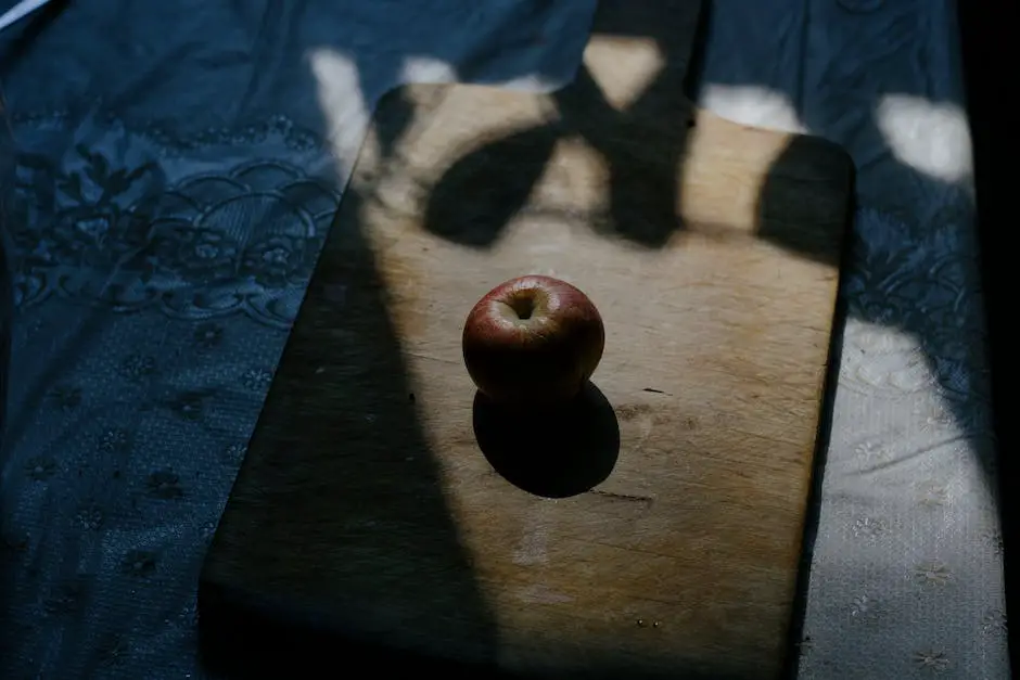 A picture of a red and green apple on a wooden table with a person smiling in the background.