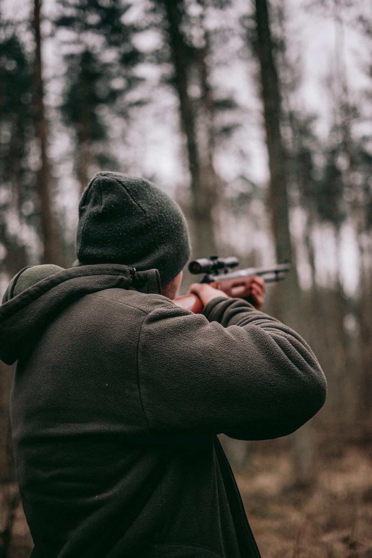 An image of a hunter standing near a tree stand in a forest, looking out for a deer.