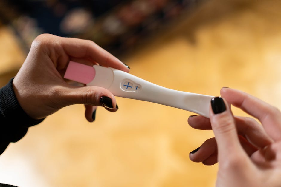 A woman holds a pregnancy test in front of her stomach, indicating that she is pregnant.